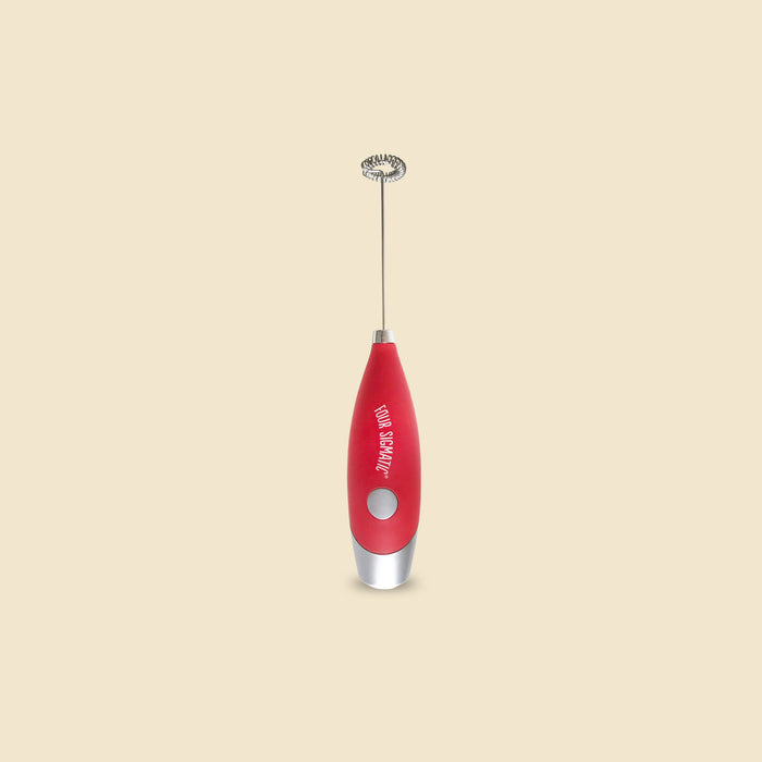 Red handheld milk frother with silver whisk against a beige background.